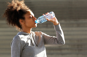 woman stands outside in sun with eyes closed drinking water
